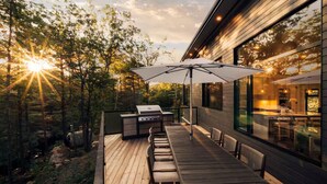 Una terraza exterior con mesa y sillas de madera, una parrilla y una sombrilla.