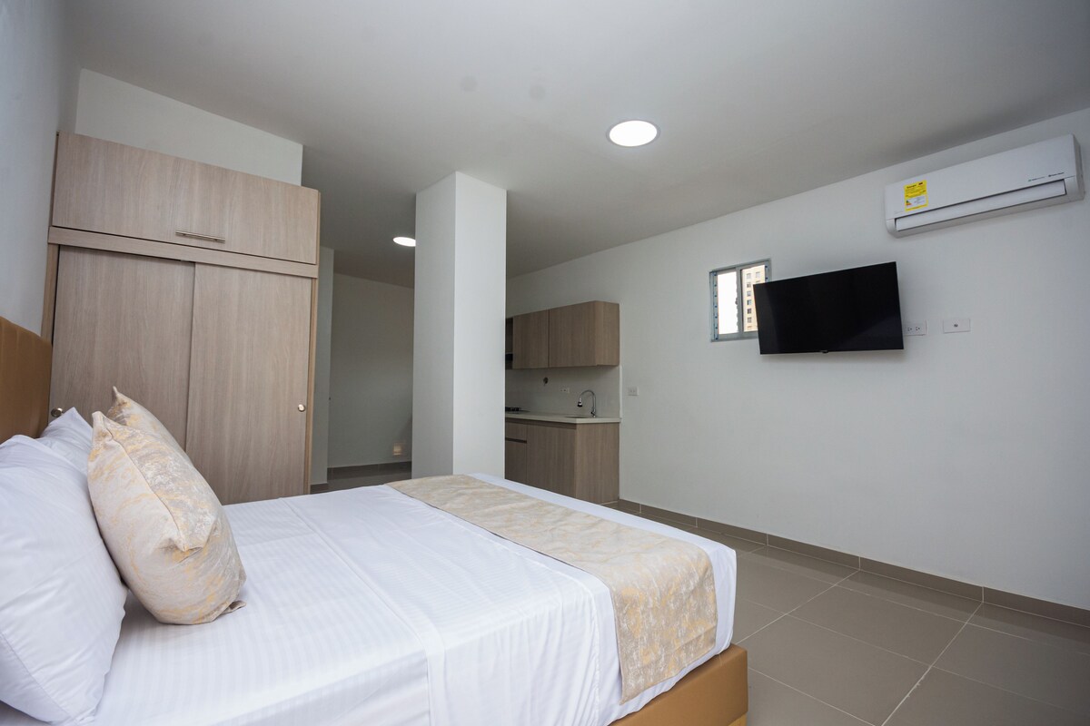 Een hotelkamer met een bed, een televisie, airconditioning en een kitchenette op de achtergrond.