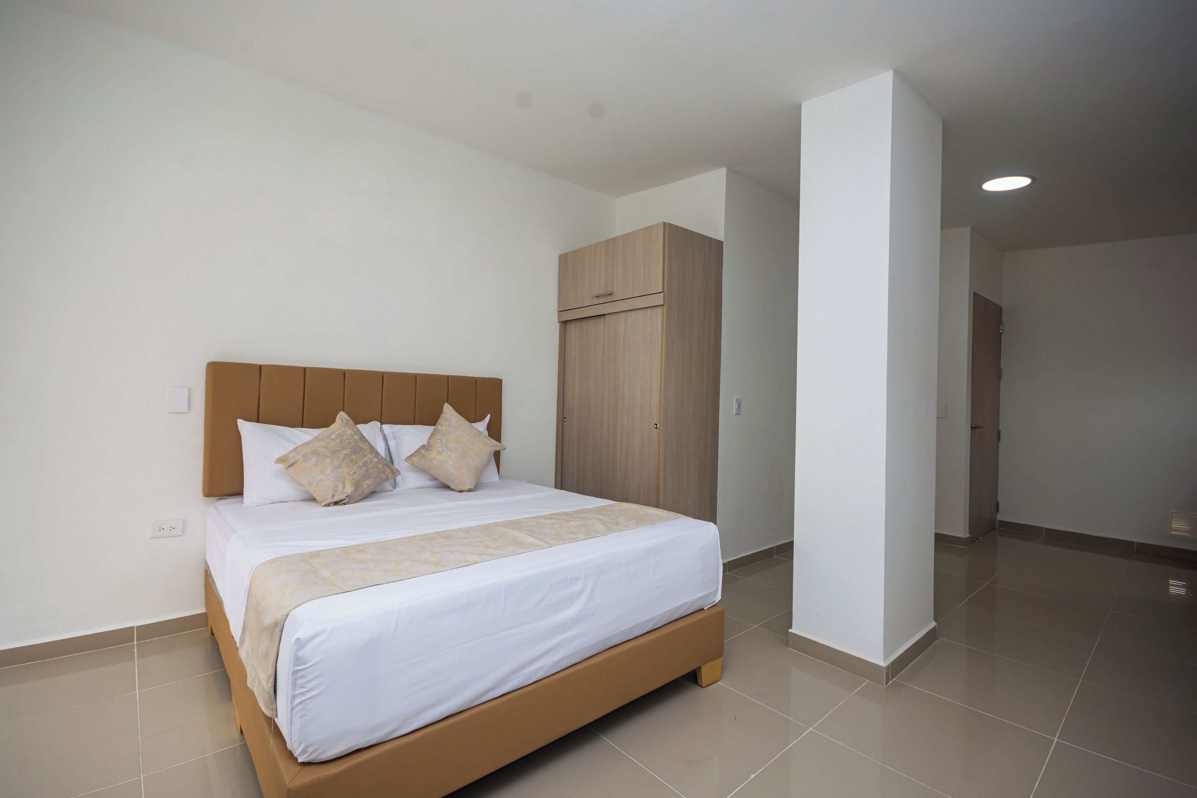 Una cama bien hecha con cabecera de madera y dos almohadas, un armario de madera y un piso de baldosas impecable en una habitación de hotel.