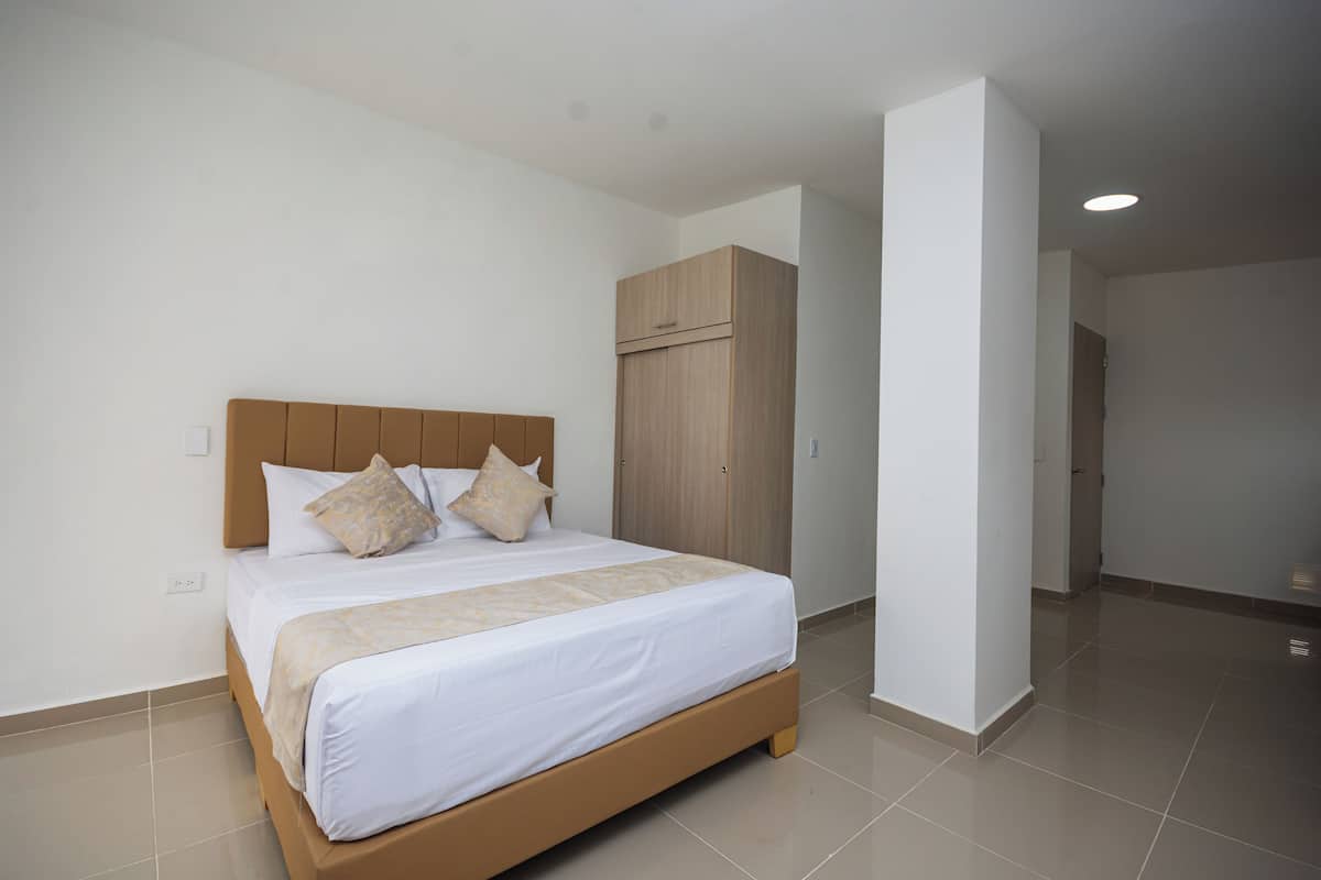 A neatly made bed with a wooden headboard and two pillows, a wooden wardrobe, and a clean, tiled floor in a hotel room.