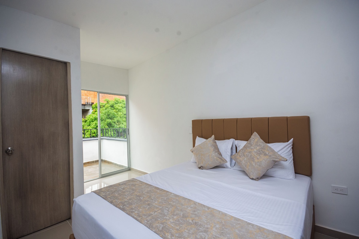 A bedroom with a large bed, a wooden door, and a view of greenery outside.