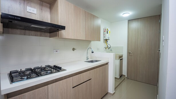 Una cucina moderna con piano cottura a gas, ripiani in marmo bianco, mobili in legno e forno integrato, oltre a un lavello in acciaio inossidabile.