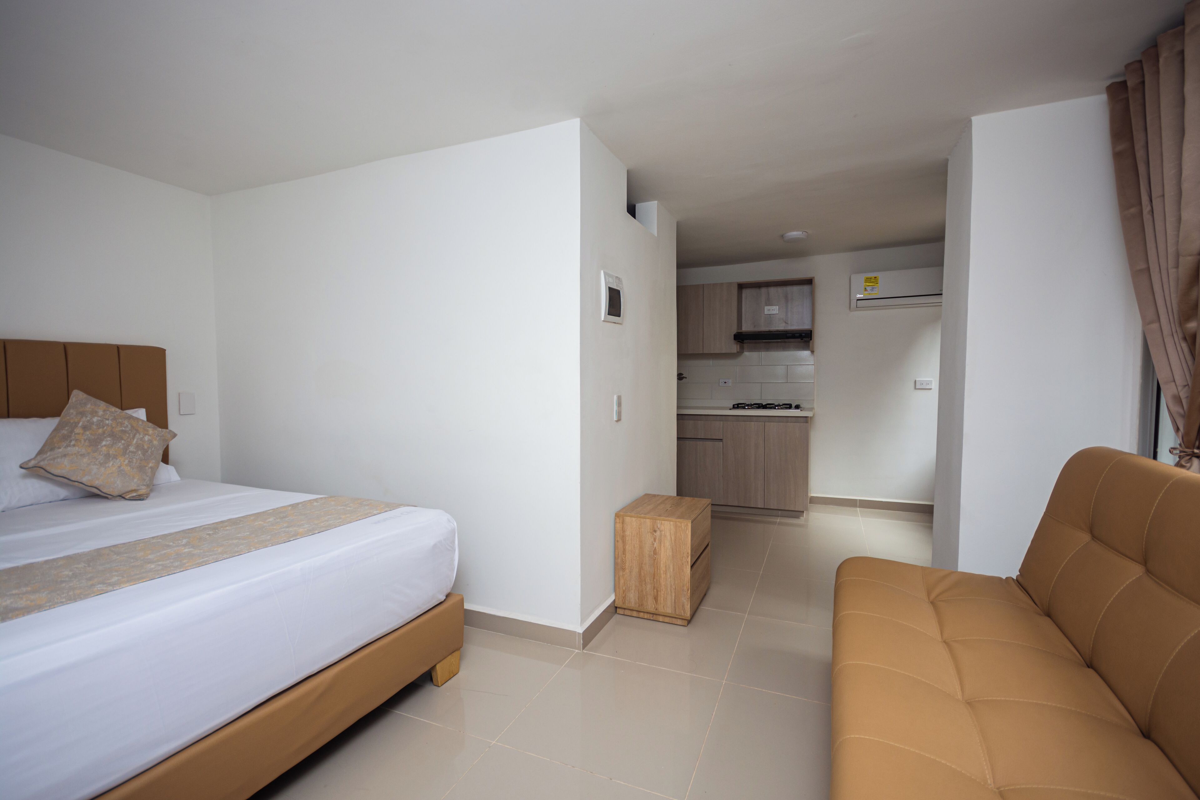 Un dormitorio con cama, mesita de noche de madera y sofá marrón.