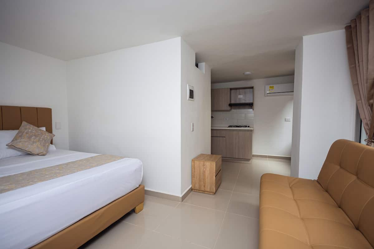 A bedroom with a bed, a wooden nightstand, and a brown sofa.