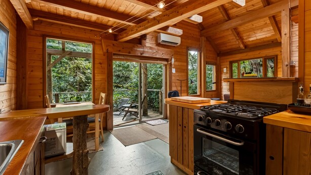 A wooden cabin with a kitchen, dining area, and large windows.