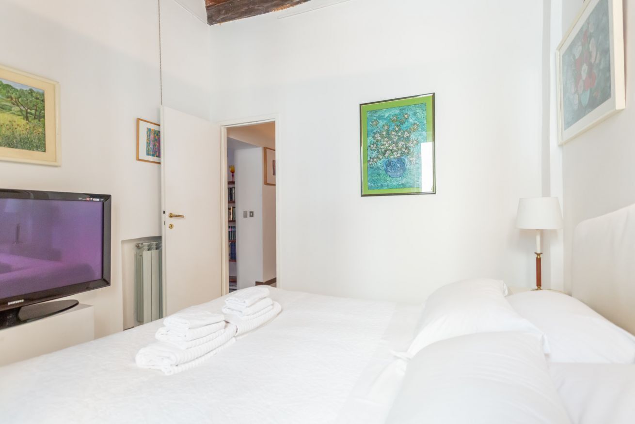 Een hotelkamer met een bed, een televisie, een schilderij en een deur die uitkomt op een gang.