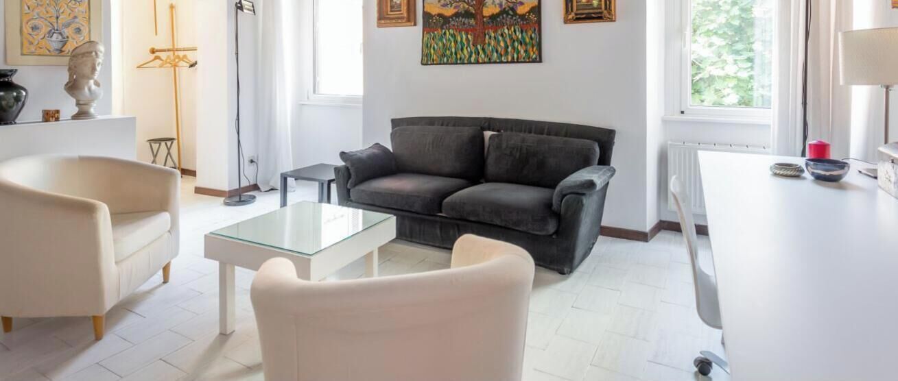 Un salon moderne avec un canapé gris, un fauteuil blanc, une table basse en verre et une table à manger blanche.