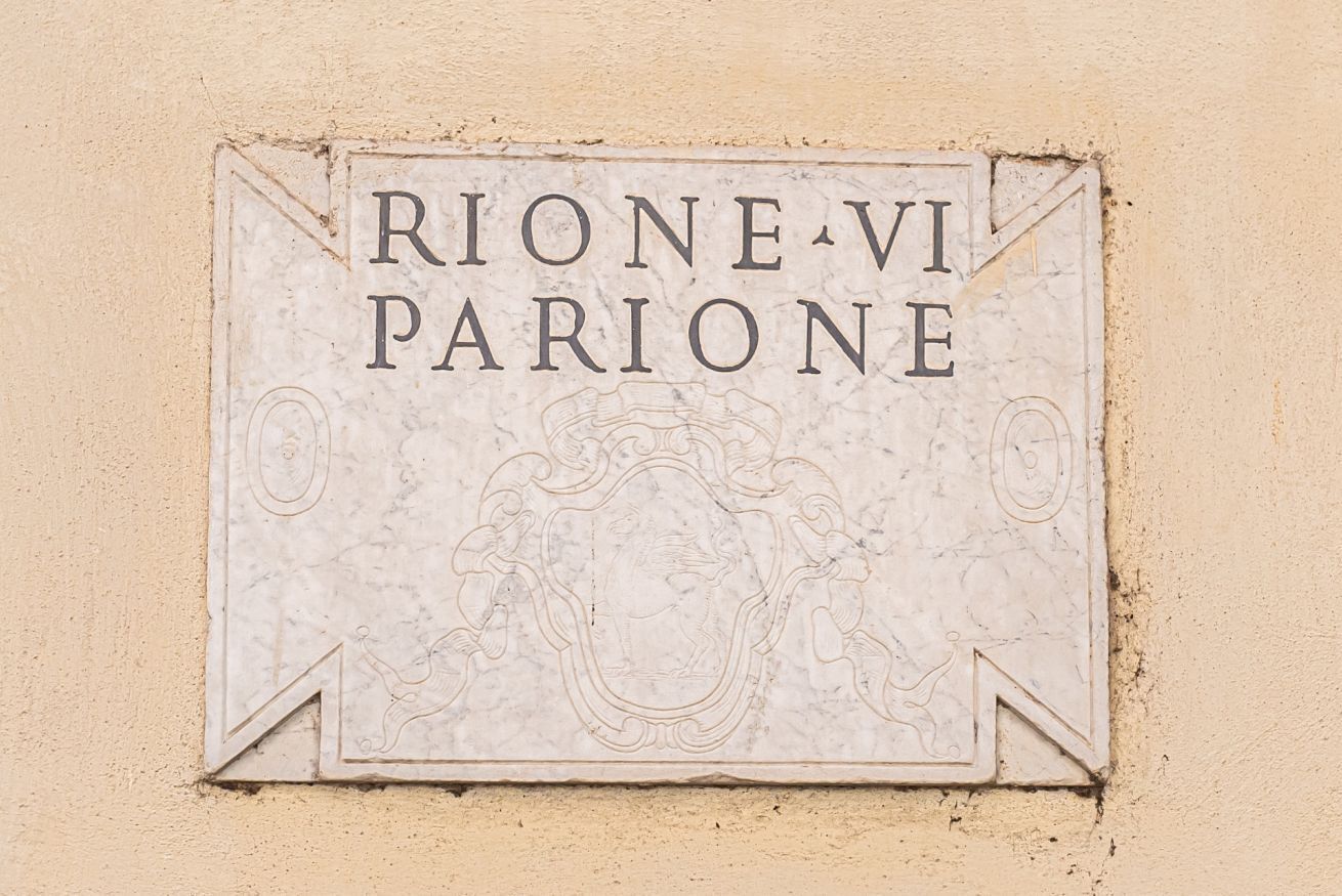 Una señal con la inscripción 'RIONE-VI PARIONE' sobre una pared color beige.
