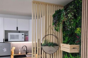 Cocina moderna con armarios blancos, microondas y pileta. Hay un separador de madera con listones verticales y un jardín vertical en la pared.