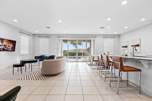 A spacious living area with a large TV, a pool view, and a dining area with chairs and a bar. - 4BR house with pool table near Disney (Kissimmee)
