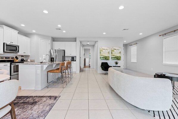 A modern kitchen with white cabinets, stainless steel appliances, and a central island with bar stools. - 4BR house with pool table near Disney (Kissimmee)
