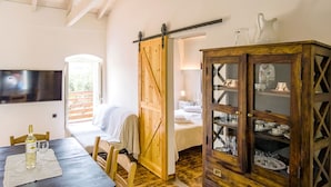 A room with a wooden dining table, chairs, a TV mounted on the wall, a sliding barn door, and a cabinet with glass doors. - Villa Adamantia in Ozias (Paxos)