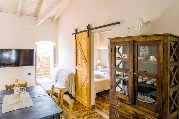 A room with a wooden dining table, chairs, a TV mounted on the wall, a sliding barn door, and a cabinet with glass doors. - Villa Adamantia in Ozias (Paxos)