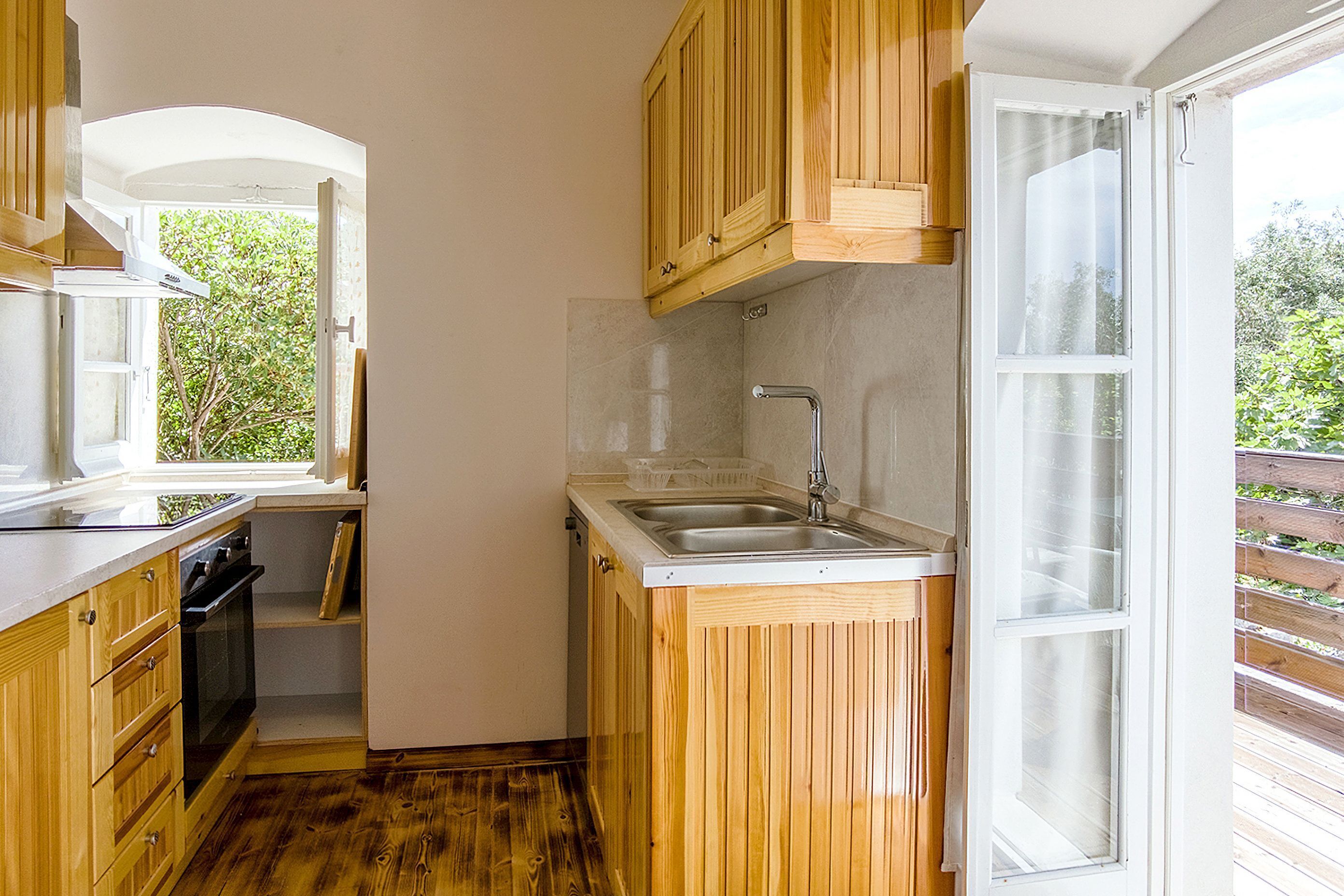 A compact kitchen with wooden cabinets, a built-in oven, and a window providing a view of greenery outside.