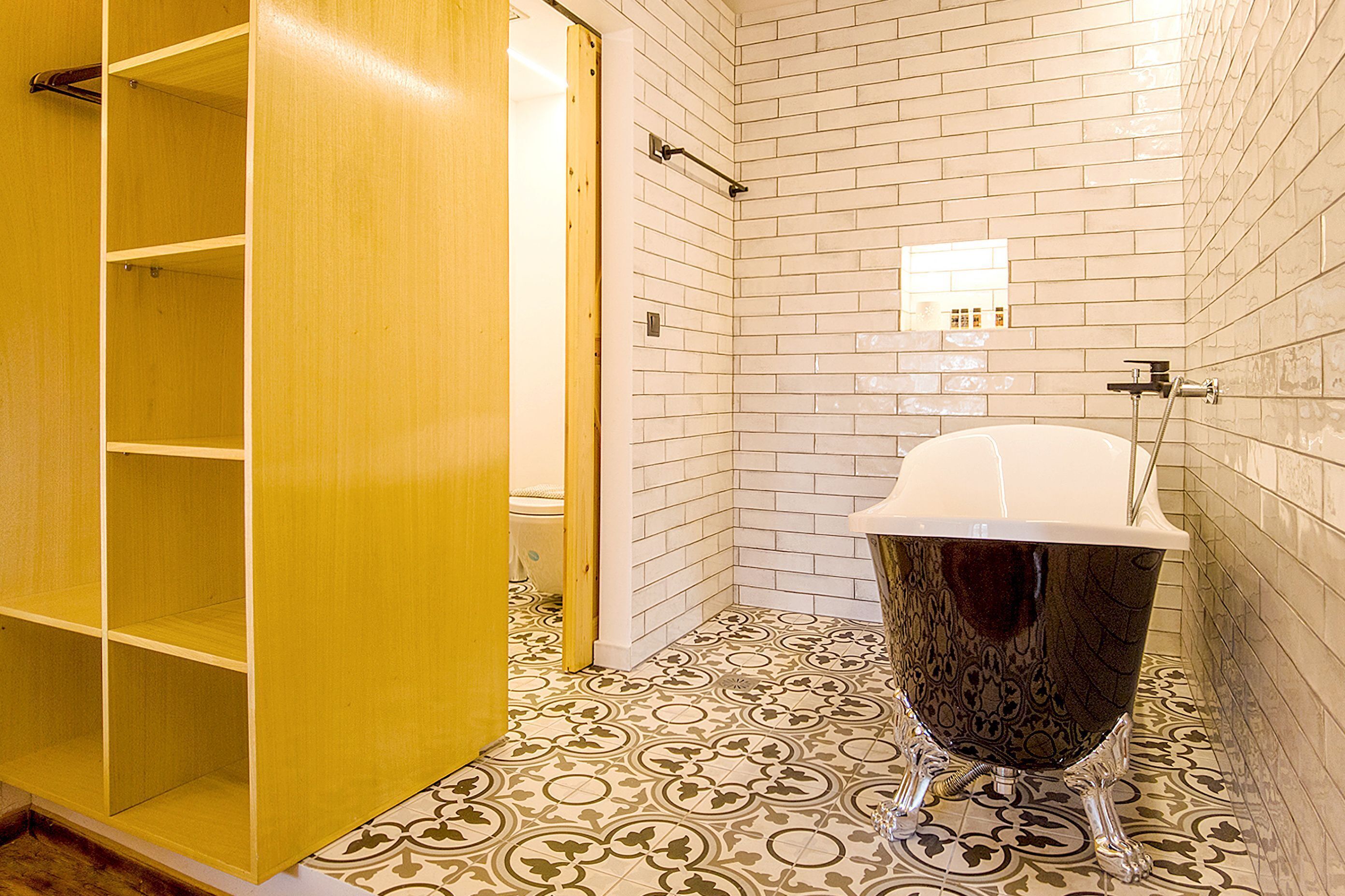 A bathroom with a white bathtub, patterned floor tiles, and a wooden wardrobe.