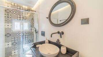 A bathroom with a patterned tile wall, a round mirror, a black countertop, and a white sink.