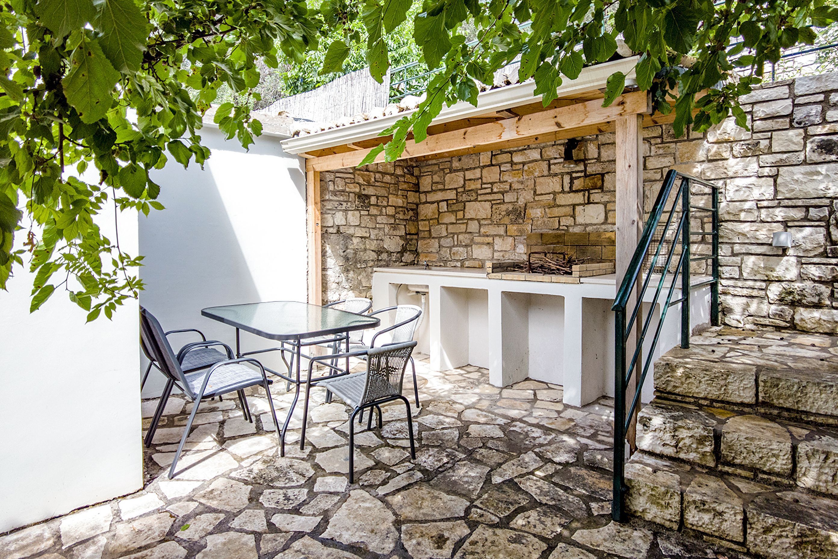 An outdoor patio with stone flooring, a glass table, metal chairs, and a stone wall.
