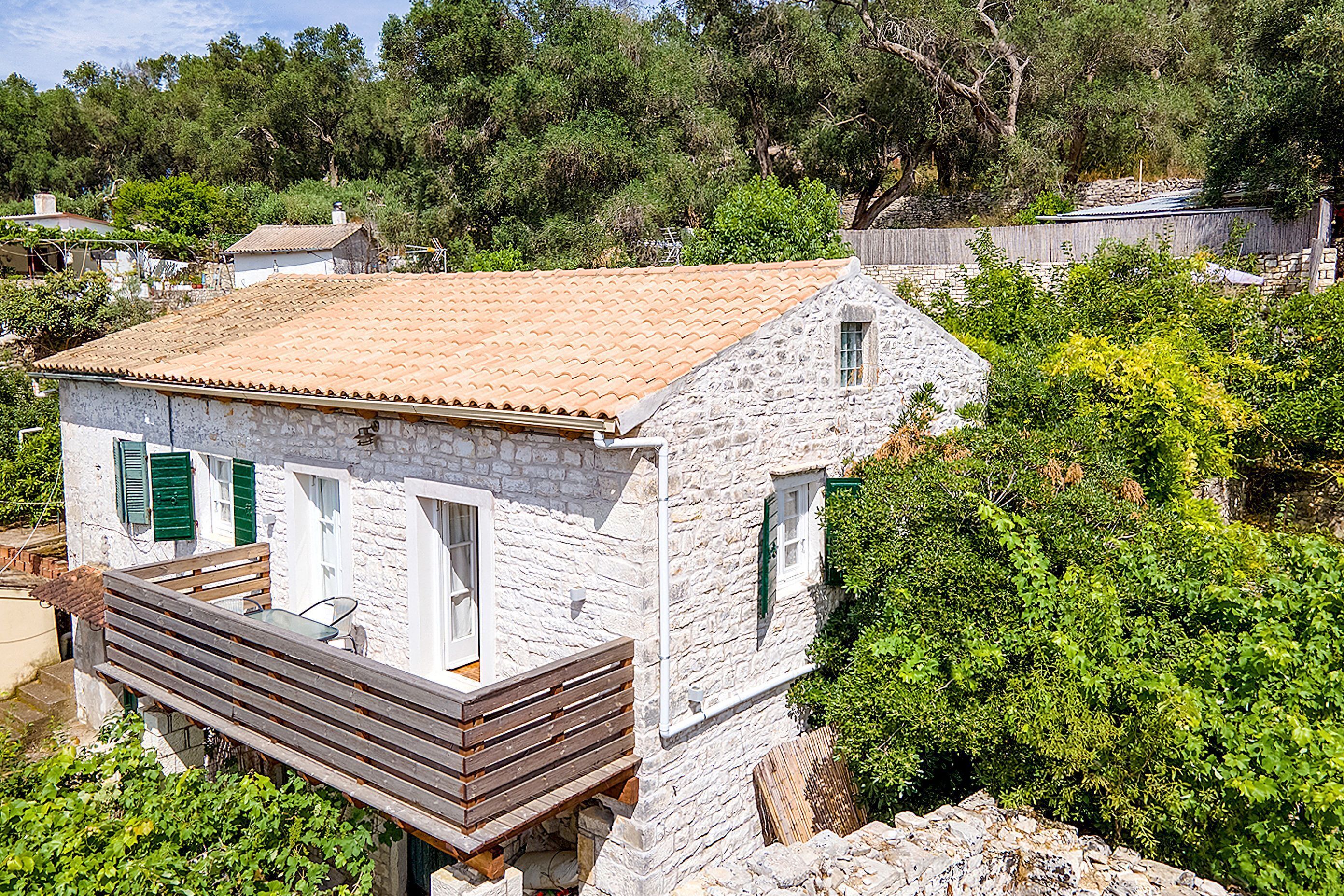 Un bâtiment en pierre avec un toit en tuiles, une terrasse en bois et des volets verts.