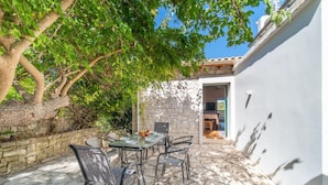 A patio with a stone table and chairs, a tree providing shade, and a view of the interior through an open doorway. - Villa Adamantia in Ozias (Paxos)