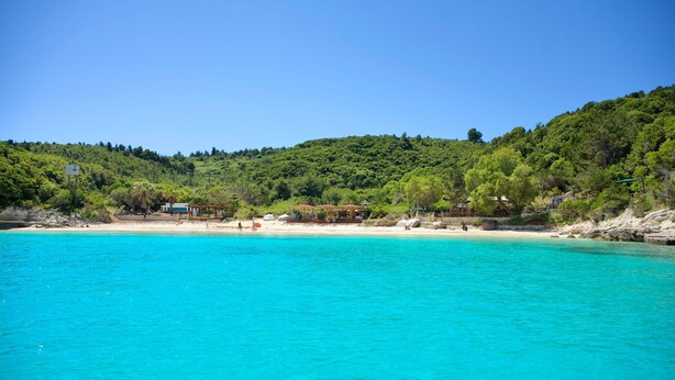 A coastal area with clear turquoise waters, a sandy beach, and a forested hillside. - Villa Adamantia in Ozias (Paxos)