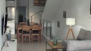 A modern living room with a grey sofa, a wooden dining table, and a staircase leading to an upper floor.