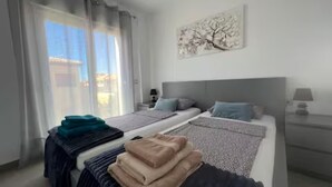 A modern bedroom with a bed, a nightstand, a lamp, and a window with curtains.