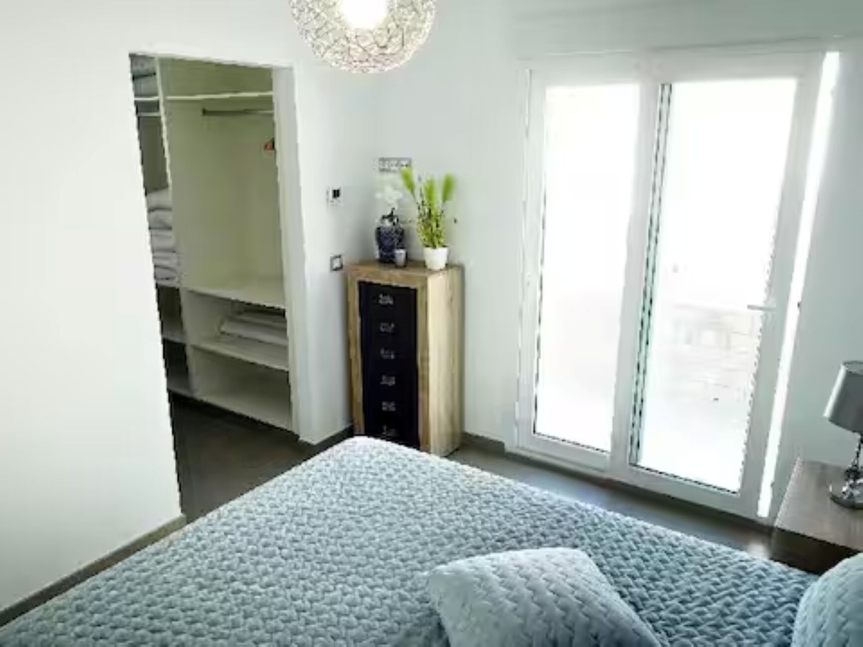 Ein Schlafzimmer mit einem Bett, einer Kommode, einer Pflanze und einer Schiebetür.