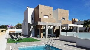 A modern two-story house with a swimming pool, outdoor seating, and a well-maintained lawn.