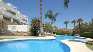 A swimming pool with a curved edge, surrounded by palm trees and a building with balconies.