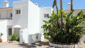 A white building with a gated entrance, potted plants, and a clear blue sky.