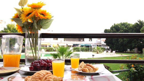 Ein Frühstückstisch mit Croissants, Trauben, Orangensaft und einer Vase mit Sonnenblumen.
