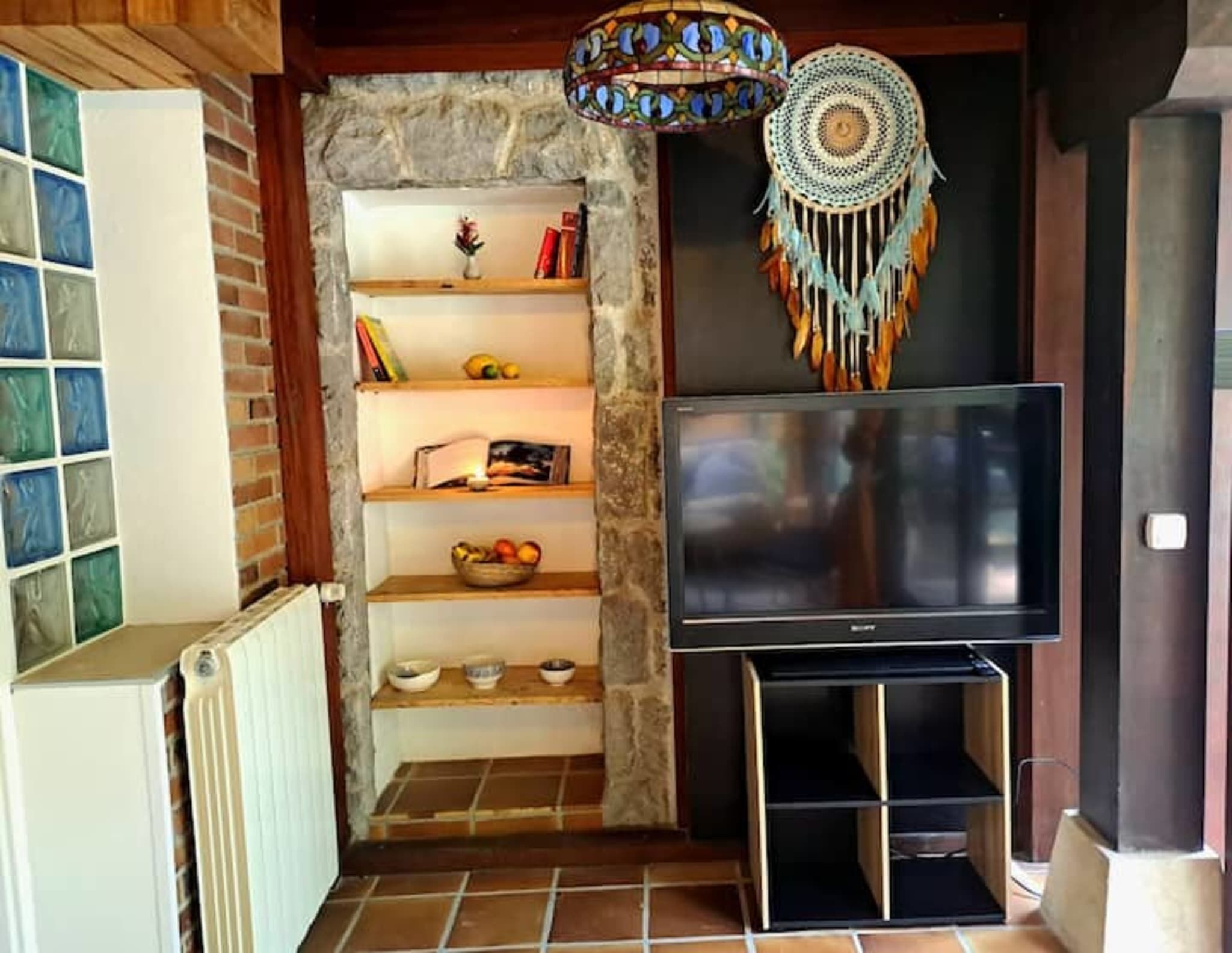 Una sala de estar con una pared de piedra, una estantería, un televisor de pantalla plana y un atrapasueños decorativo.