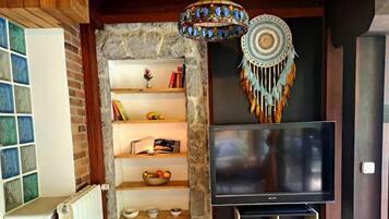 Una sala de estar con una pared de piedra, una estantería, un televisor de pantalla plana y un atrapasueños decorativo.