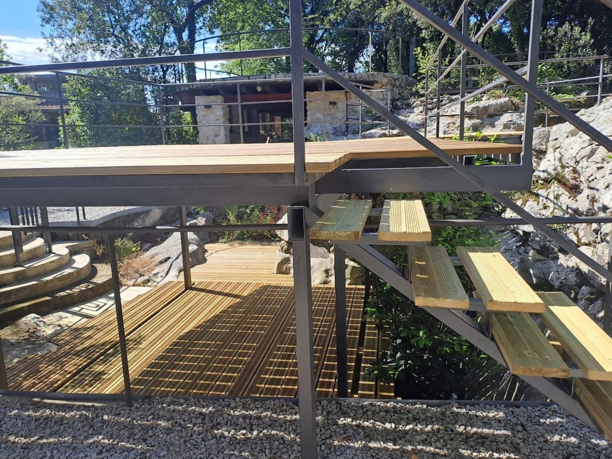Eine Holzterrasse mit Metallgeländern, umgeben von felsigem Gelände und Bäumen.