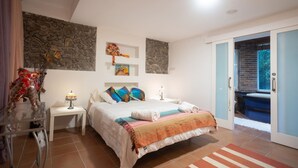 A bedroom with a bed, nightstands, a lamp, a stone wall, and a door leading outside. - Inspiring Loft in the forest. Armonía Natura House (Camargo)
