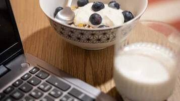 Ein Laptop auf einem Holztisch zusammen mit einer Schüssel Müsli und einem Glas Milch.