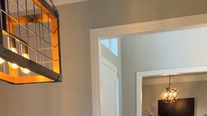 A dining area with a wooden table and white upholstered chairs, a potted plant, and a hanging light fixture. - Luxury 4,300 SqFt Home • Sleeps 12 • Outdoor Kitchen & Patio with Large Pool (Colleyville)