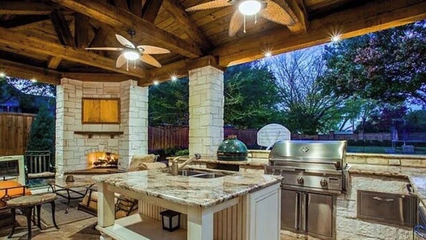 An outdoor kitchen with a stone fireplace, a grill, and a sink. - Luxury 4,300 SqFt Home • Sleeps 12  • Outdoor Kitchen & Patio with Large Pool (Colleyville)