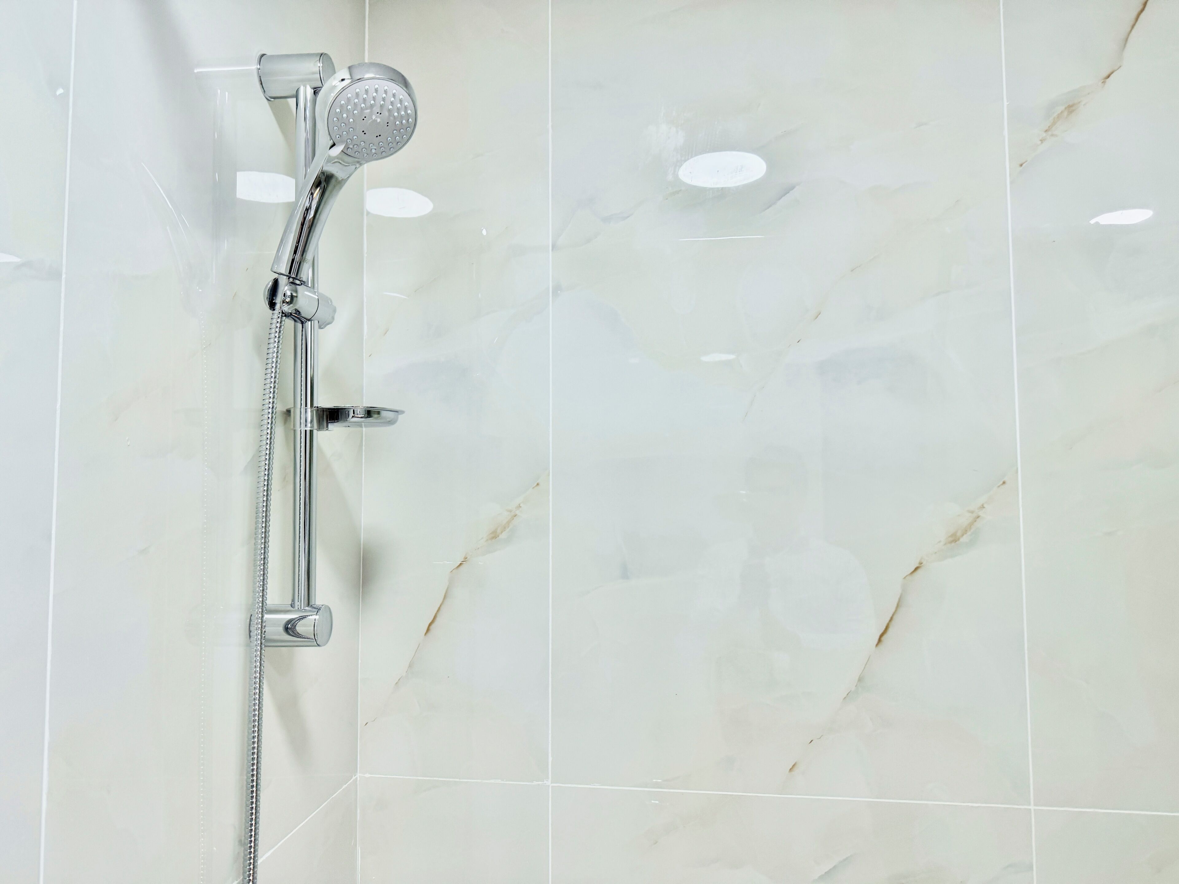 Doccia con soffione estraibile e flessibile, fissato a una parete con piastrelle dall'effetto marmo.