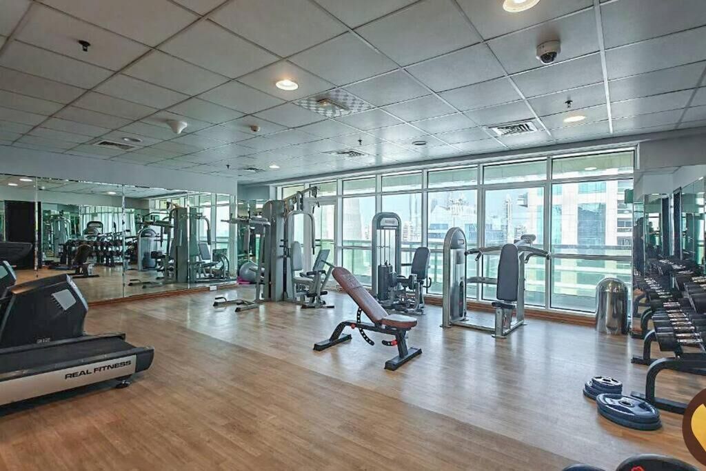 Une salle de sport spacieuse, dotée de divers appareils d’exercice, de grandes fenêtres et d’un plancher en bois.