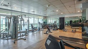 Kuntosali, jossa on monenlaisia kuntoilulaitteita, suuret ikkunat ja piano.