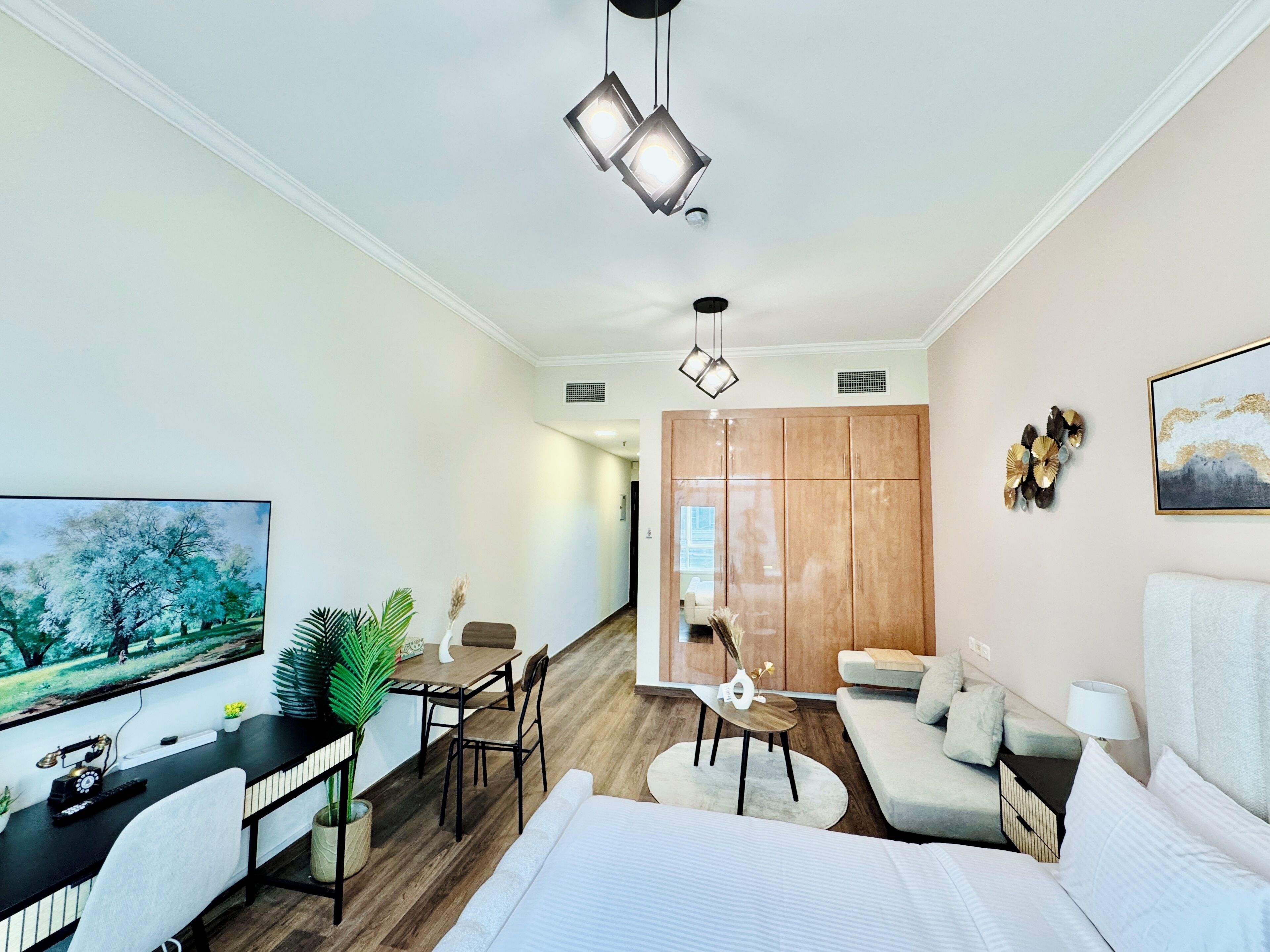 A modern hotel room with a bed, a desk, a dining area, and a view of the city.