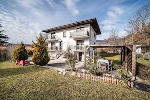 Ein modernes, zweistöckiges Haus mit Balkon, Holzterrasse und umzäunter Garten.