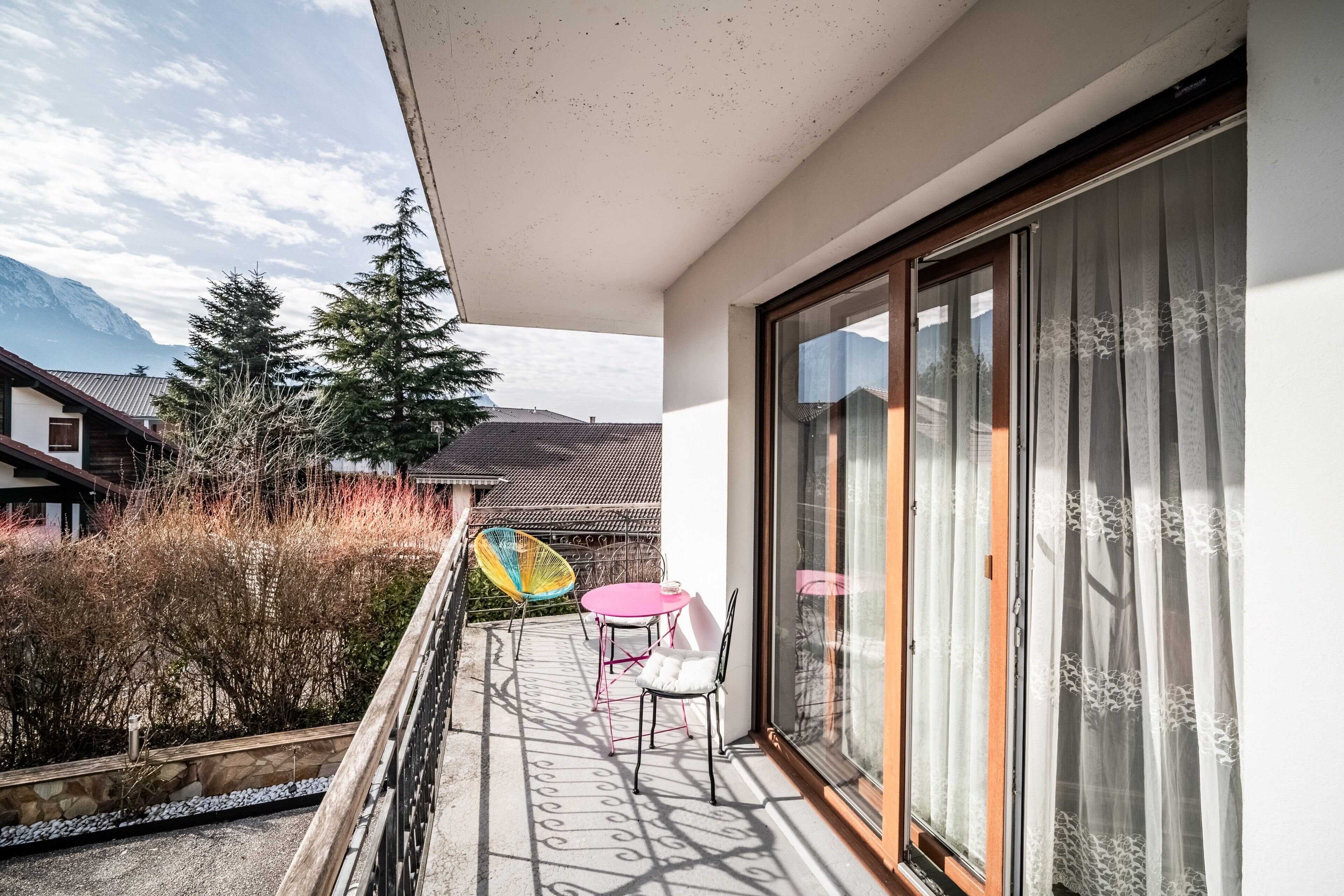 Un balcon avec une table et des chaises, une vue sur une montagne et un bâtiment doté d’un toit en pente.
