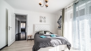 A bedroom with a bed, a chandelier, a view of a cityscape, and a door leading to another room. - Villa "L'Oranaise" – 190 m², Mountain View, Private Balconies, Terraces & Garden (Cluses)