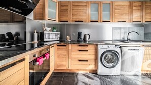 A modern kitchen with wooden cabinets, a built-in oven, a washing machine, and a stainless steel countertop. - Villa "L'Oranaise" – 190 m², Mountain View, Private Balconies, Terraces & Garden (Cluses)