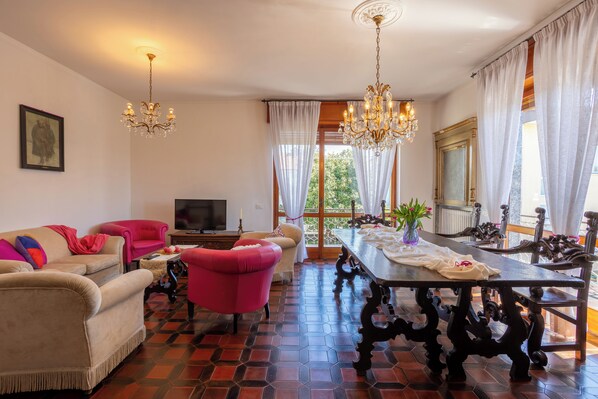 Un salon comprenant un canapé, des fauteuils, un téléviseur, une table à manger et un lustre.