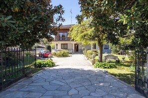 A stone-paved pathway leading to a house with a balcony, surrounded by greenery and a fenced garden. - Villa Gabri 1 e 2 (Arona)