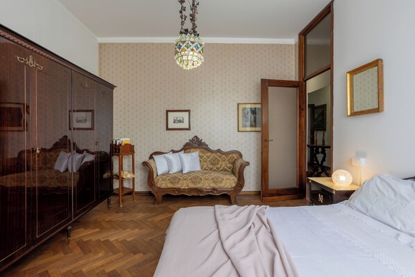 A bedroom with a large wardrobe, a sofa, a bed, and a mirror.