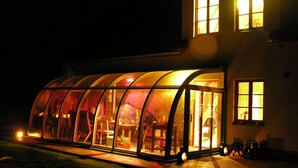 Una estructura con paredes de vidrio donde se ve un comedor en su interior, junto a un edificio con ventanas.